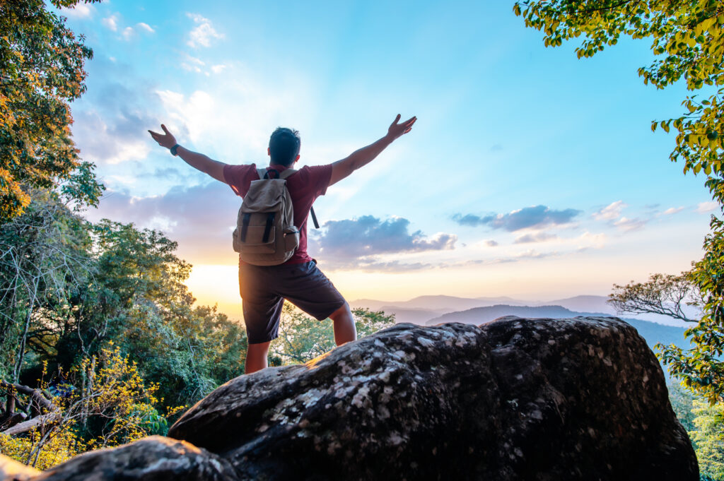 Young trekking man standing on rocky mountain peak
